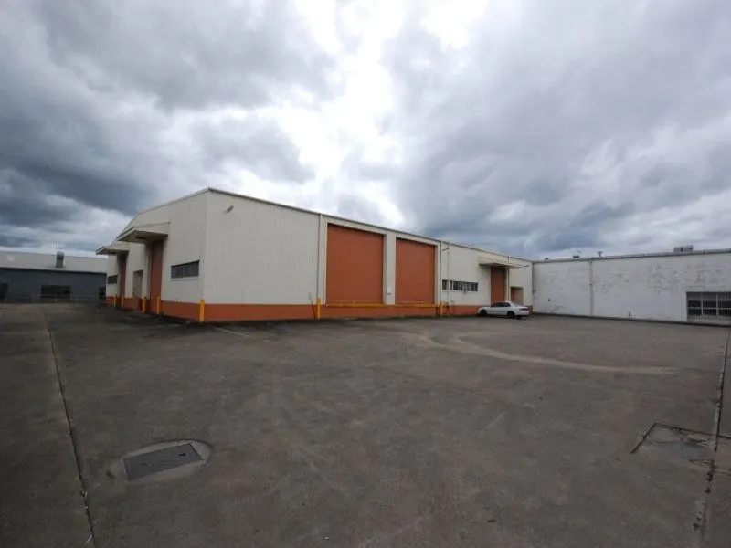 Exterior of an industrial warehouse with roller doors and a large concrete yard